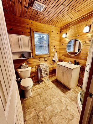 A wooden-paneled bathroom with a toilet, sink, and mirror.
