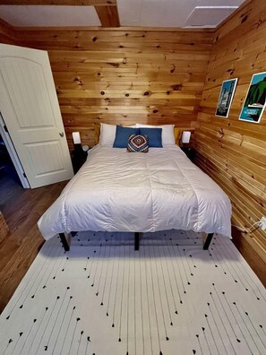A wooden-paneled room with a bed, a white door, and a wall with framed pictures.