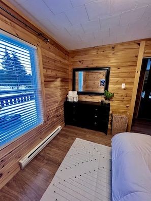 A wooden-paneled room with a bed, a dresser, a mirror, and a window with blinds.