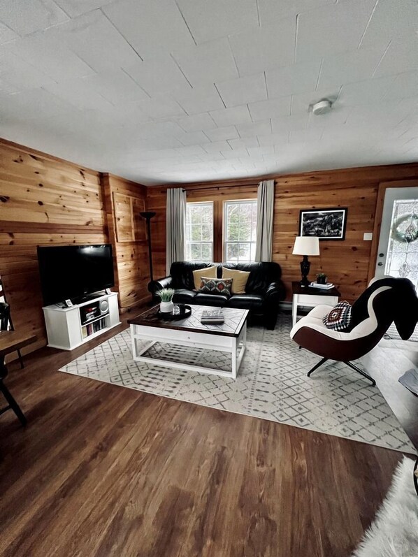 A wooden-paneled room with a sofa, a coffee table, a TV, and a lamp.