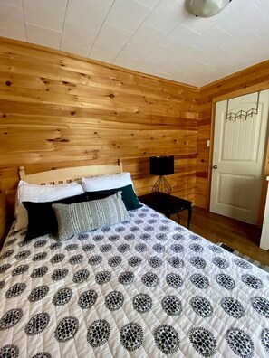 A wooden-paneled room with a bed, a small table, and a door.