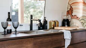 A kitchen with a window, wooden cabinets, a sink, and a kettle.