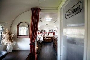 A compact RV interior with a visible bed, a small window, and a sign indicating a washroom. - 1971 Vintage Modern Airstream with Cowboy Tub (deseronto)