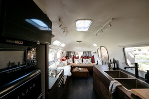 Ein kompaktes Wohnmobil-Interieur mit einer Küchenzeile, einer Sitzecke mit Kissen und einem kleinen Fenster.