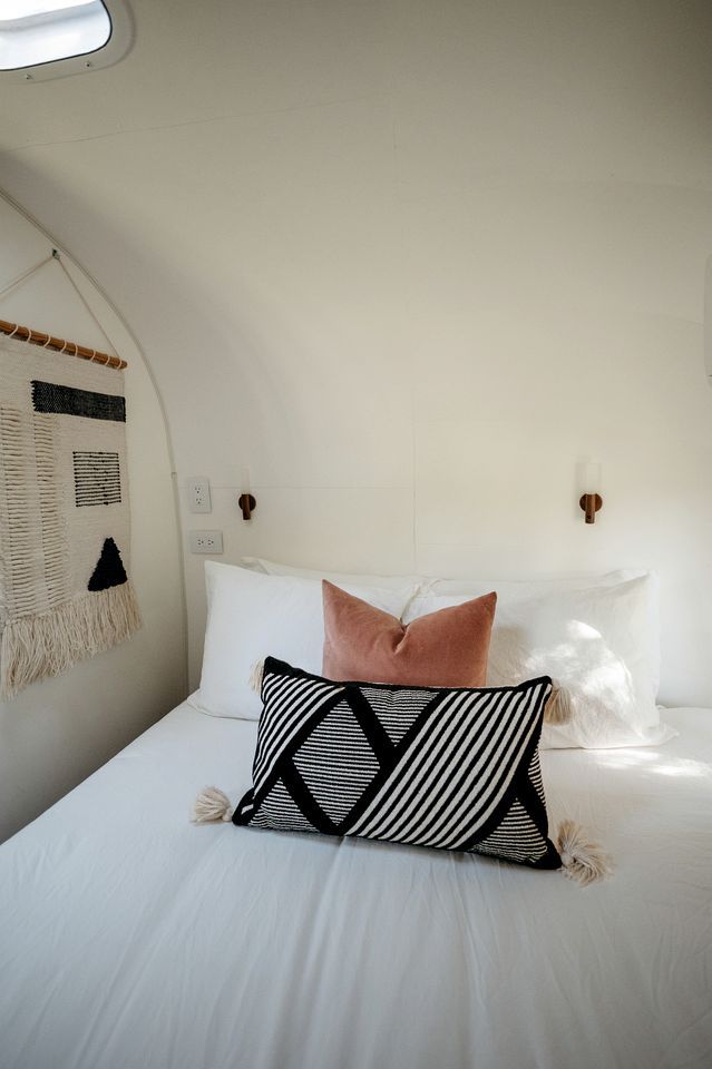 A bed with white bedding, a black and white striped pillow, and a pink pillow.