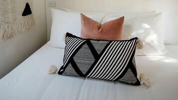 Ein Bett mit weißer Bettwäsche, einem schwarz-weißen Kissen und einem rosafarbenen Kissen.