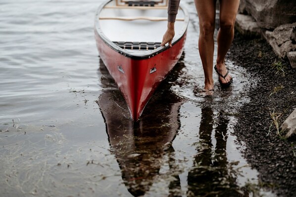 Une personne se tient à côté d’un bateau rouge sur une surface mouillée.