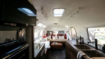 A compact RV interior with a kitchenette, a seating area with cushions, and a small window.