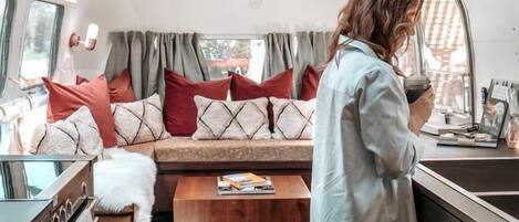 Un espace de vie compact comprenant un coin cuisine, un canapé avec des coussins, une fenêtre et une personne debout près du comptoir.