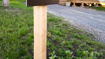 A sign with the text 'The Nomad' on a wooden post in a grassy area with trees and a wooden structure in the background.