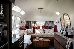 A cozy RV interior with a kitchenette, a seating area with cushions, and a dining table. - 1971 Vintage Modern Airstream with Cowboy Tub (deseronto)