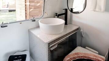 A compact bathroom with a white sink, a mirror, a towel rack, and a window.