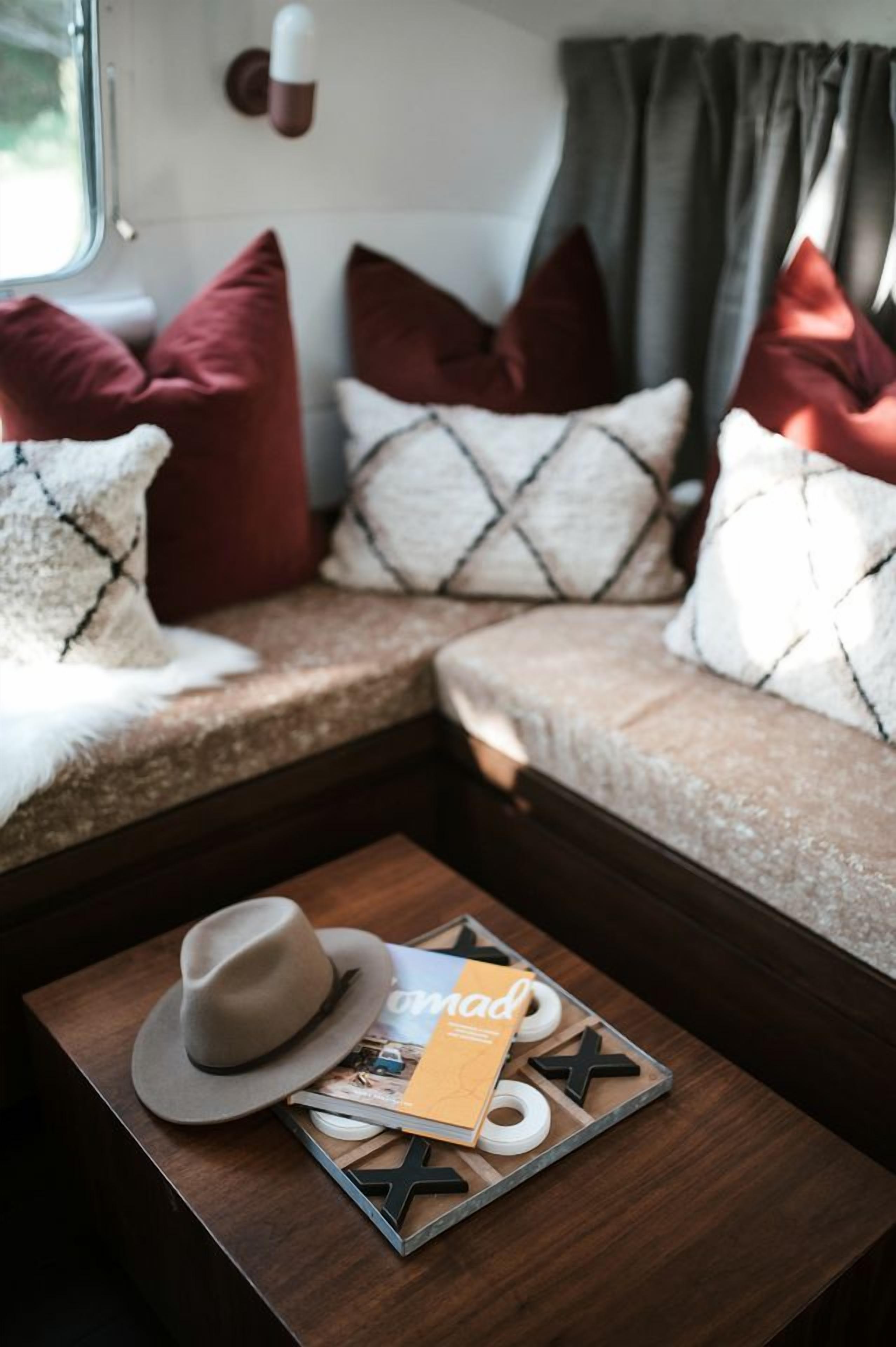 A cozy RV interior with a cushioned seating area, a small table with a hat and a magazine, and a window with curtains.