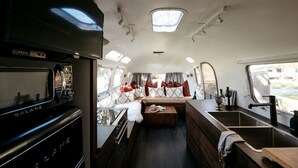 Ein kompaktes Wohnmobil-Interieur mit einer Küchenzeile, einer Sitzecke mit Kissen und einem kleinen Fenster.