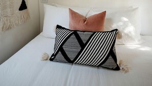 A bed with white bedding, a black and white striped pillow, and a pink pillow.