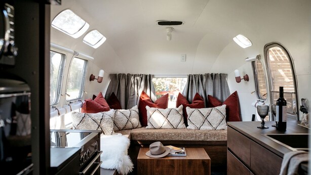 A cozy RV interior with a kitchenette, a seating area with cushions, and a dining table.