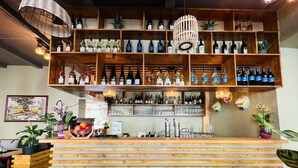 Zona de bar con estanterías de madera que exhiben diferentes botellas, una barra con frutero y plantas decorativas.