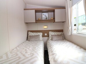 A small room with two beds, a mirror, a shelf with decorative items, and a window with curtains. - 18 Eden Heights (St. Andrews)