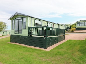 A green mobile home with a fenced deck, a large window, and a door. - 18 Eden Heights (St. Andrews)