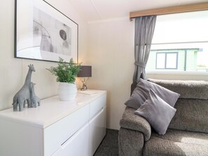 A room with a white dresser, a grey sofa, a framed abstract painting, a potted plant, a lamp, and a window with curtains. - 18 Eden Heights (St. Andrews)
