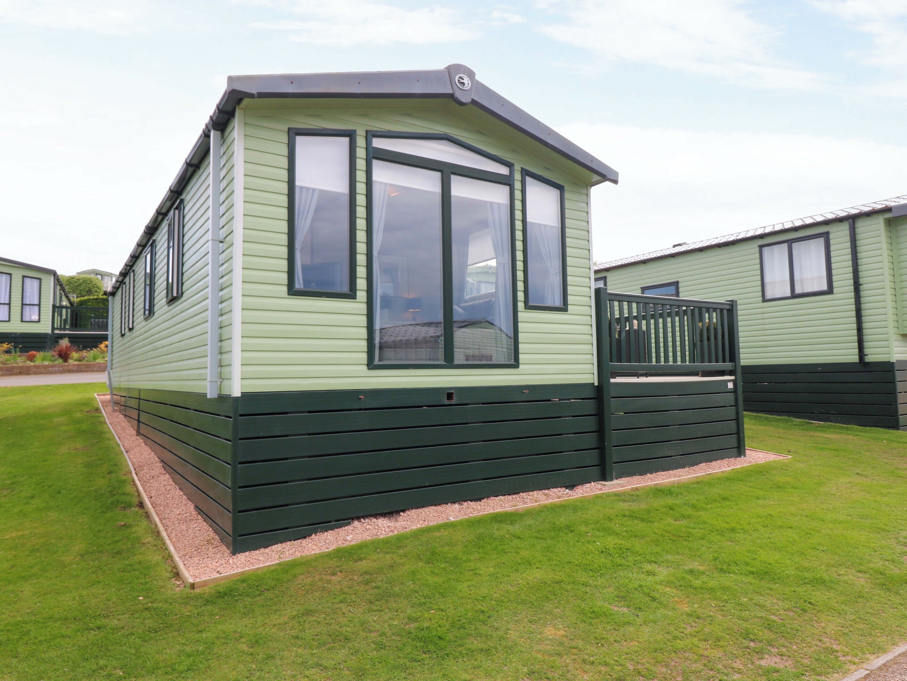 A single-story, green mobile home with a small porch and a fenced yard.