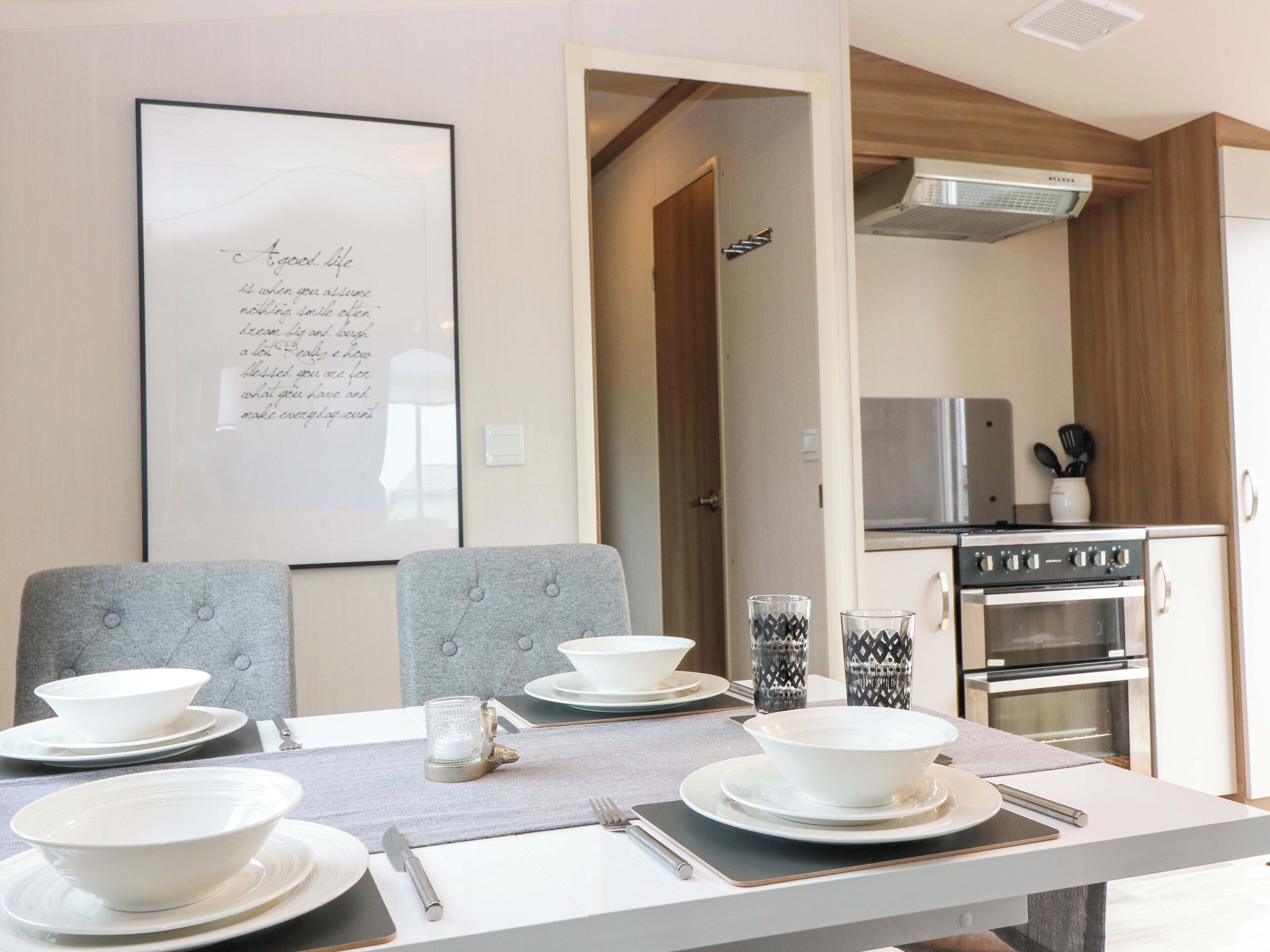 A dining area with a table set for four, a kitchen in the background, and a framed inspirational quote on the wall.