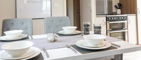 A dining area with a table set for four, a kitchen in the background, and a framed inspirational quote on the wall.