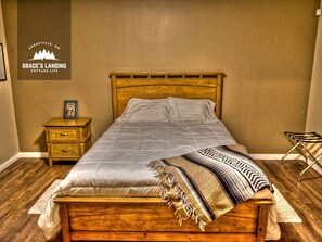 A bedroom with a wooden bed, a nightstand with drawers, a framed picture, and a sign on the wall. - Beautiful Cottage with Fire Pit and Barbecue in Belleville, Ontario (Belleville)