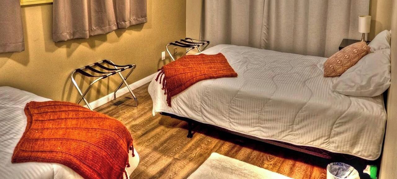 A hotel room with two beds, a wooden floor, and a nightstand with a lamp.