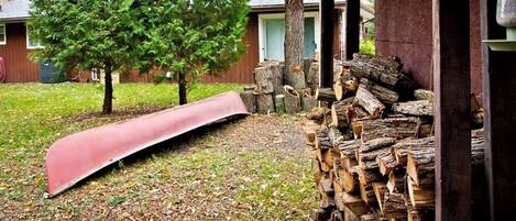 Un jardin avec un toboggan rouge, une pile de bois de chauffage et un arbre.