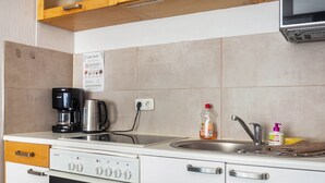 Kompakti keittiö, jossa on Siemensin astianpesukone, kahvinkeitin, hana ja pieni työtaso.