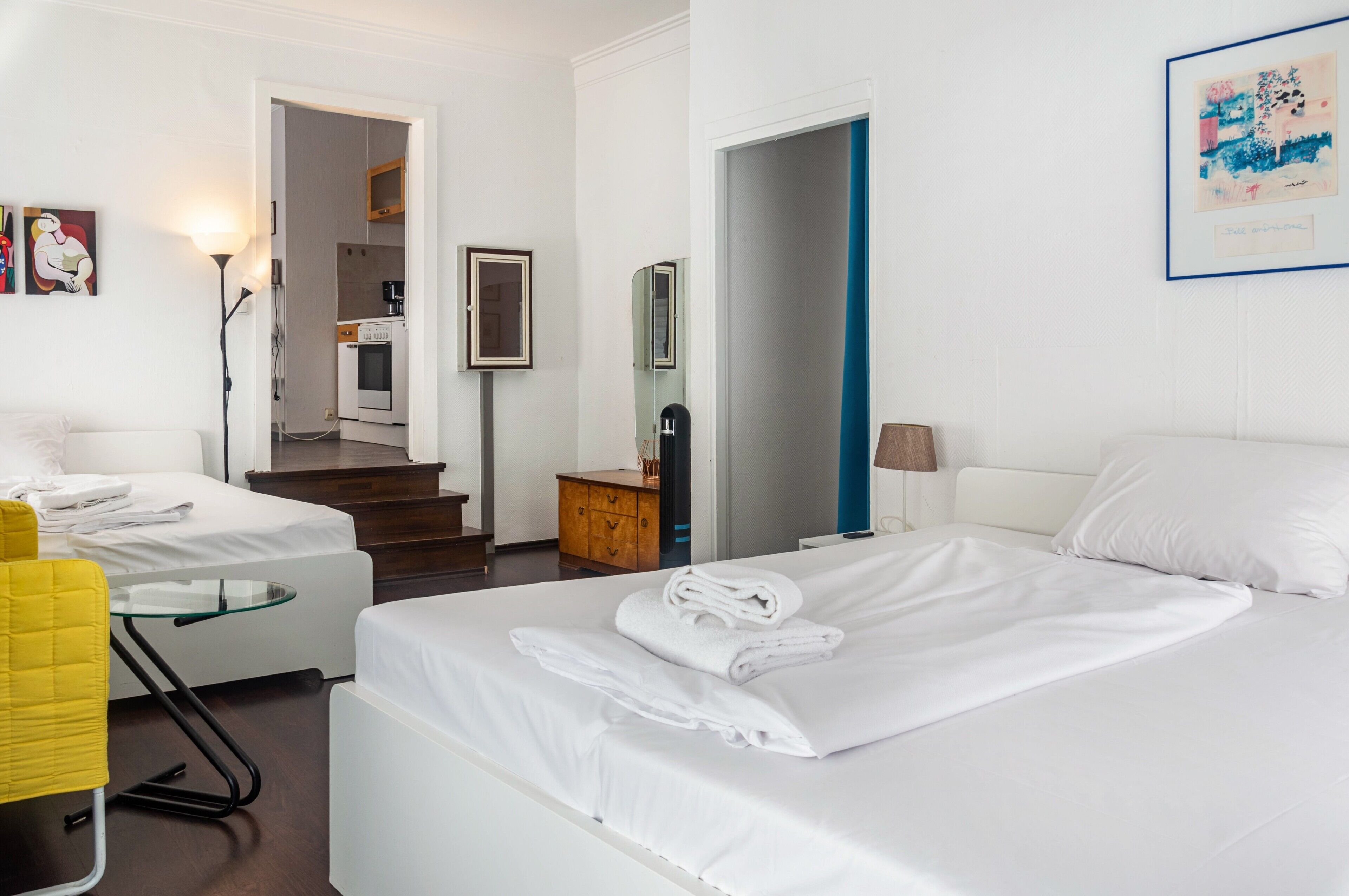 A hotel room with a bed, a desk, a chair, a wardrobe, a mirror, and a bathroom visible through an open door.