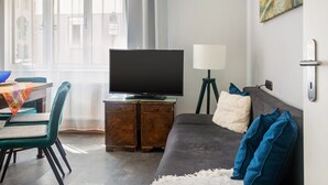 A living room with a television on a wooden cabinet, a sofa, a lamp, and a dining table with chairs.