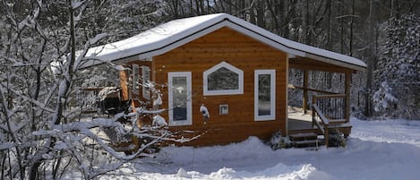 Una cabaña de madera con un porche, rodeada de árboles cubiertos de nieve.