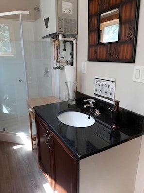 A bathroom with a black countertop sink, a mirror, and a shower area.