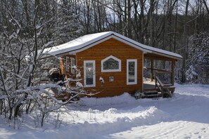 Une cabane en bois dotée d’un porche, entourée d’arbres couverts de neige.