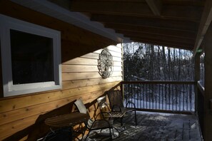 A wooden porch with a bench, a chair, and a railing.