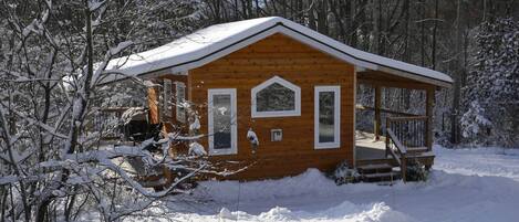 Una cabaña de madera con un porche, rodeada de árboles cubiertos de nieve.