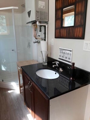 A bathroom with a black countertop sink, a mirror, and a shower area.