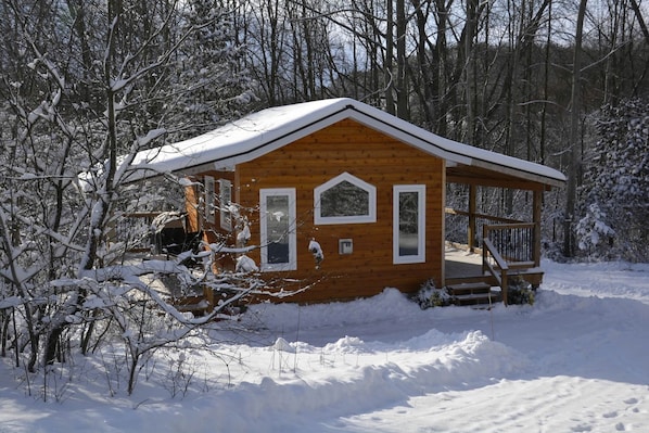 A wooden cabin with a porch, surrounded by snow-covered trees.