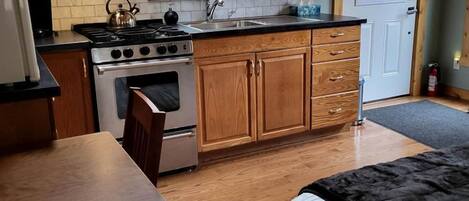 A compact kitchen with wooden cabinets, a built-in oven, a stove, and a window above the sink.