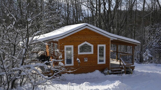 Una cabaña de madera con un porche, rodeada de árboles cubiertos de nieve.