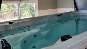Un jacuzzi en una habitación con techo de madera, una ventana con vistas a árboles y una silla.