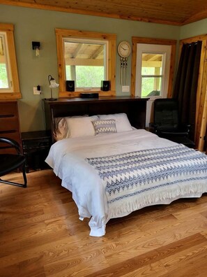 Une chambre à coucher avec une tête de lit en bois, un lit avec une literie à motifs, un bureau avec une lampe et une chaise.