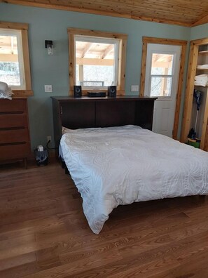 A bedroom with a wooden bed, a dresser, a desk with speakers, and a window.