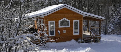 Una cabaña de madera con un porche, rodeada de árboles cubiertos de nieve.