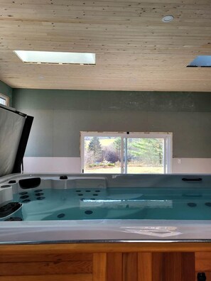 A spa room with a hot tub, wooden ceiling, and a window with a view of trees.