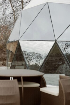 Eine moderne, geometrische Glasarchitektur mit reflektierender Oberfläche, umgeben von Sitzmöglichkeiten im Freien.