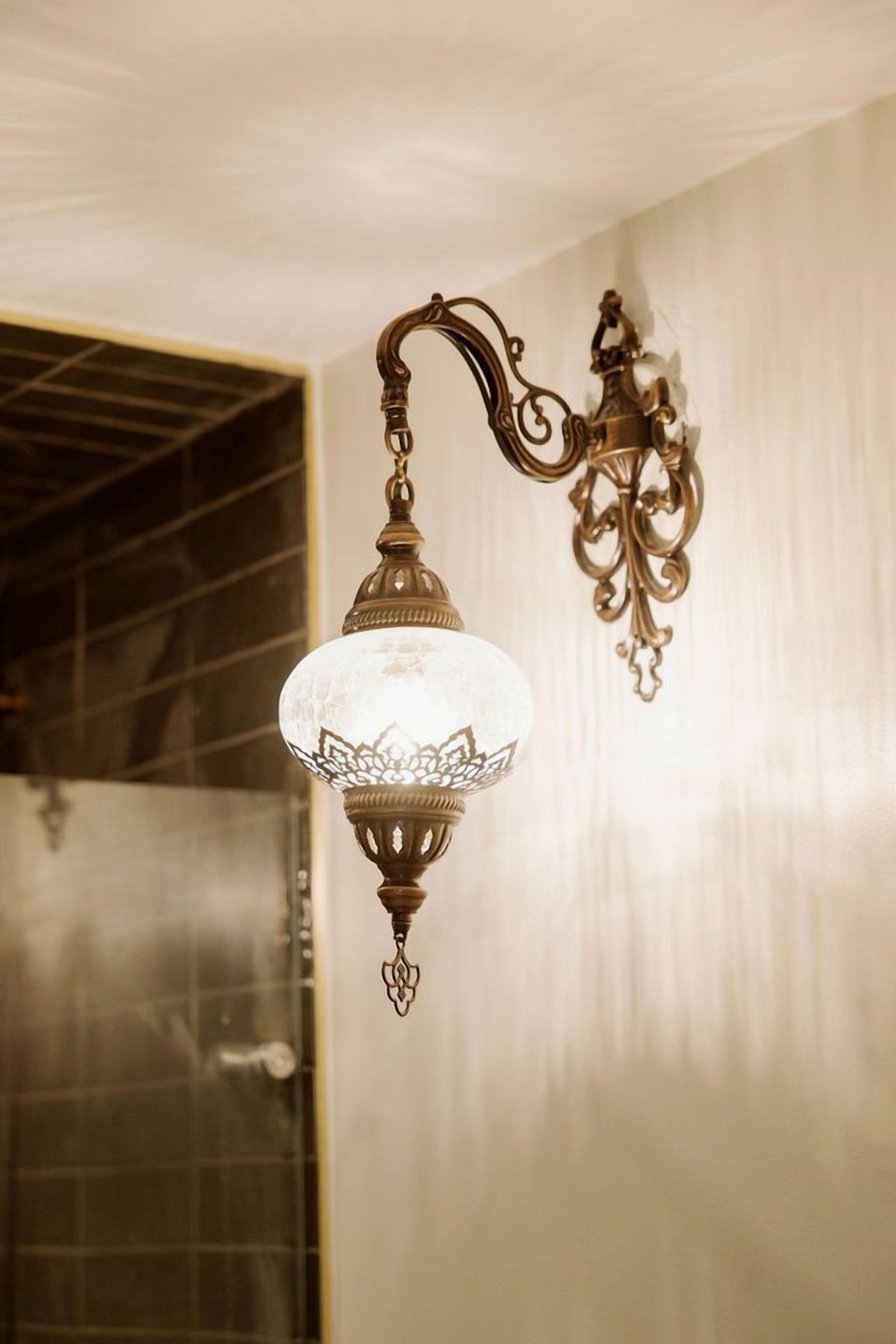 En vægmonteret lampe med glaskuplet og detaljeret metaludsmykning.