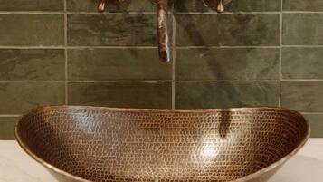 A bathroom with a copper-colored basin, green tiled walls, and three copper faucets.